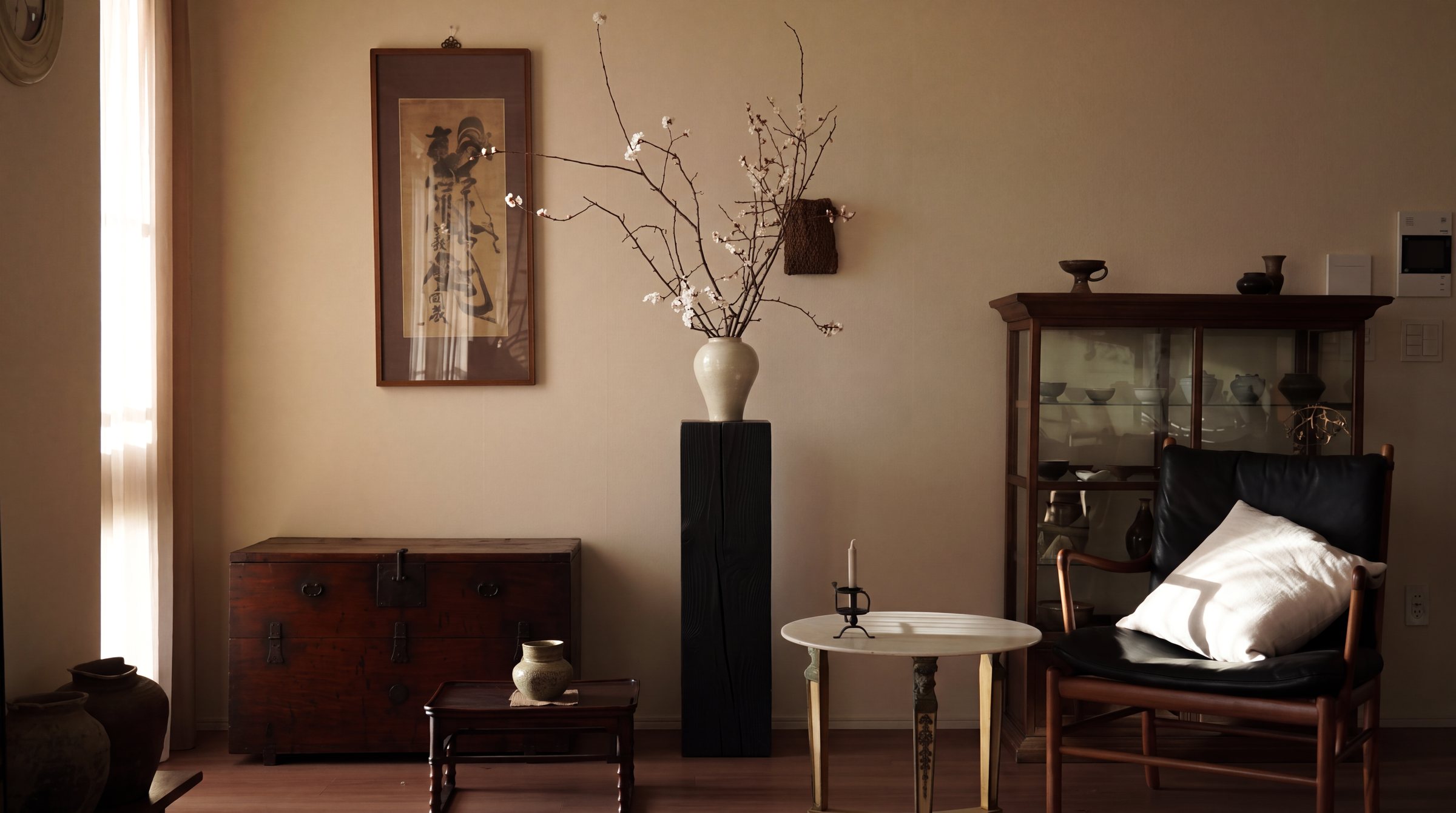 Black pedestal holding a white vase of blossom branches in a sunlit living room