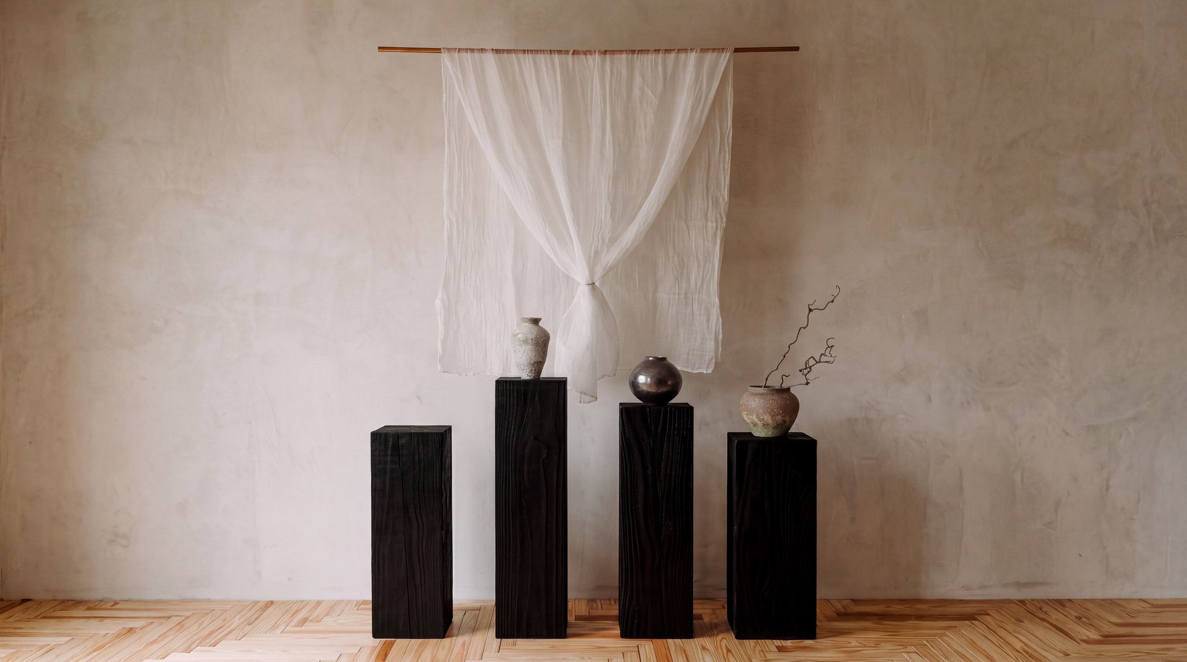 Four black pedestals of different heights beneath a sheer hanging cloth