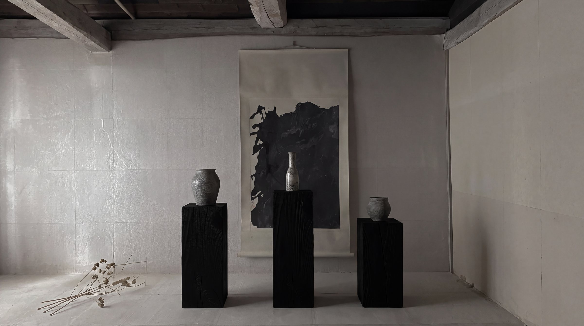 Three black pedestals with vessels in front of an ink scroll