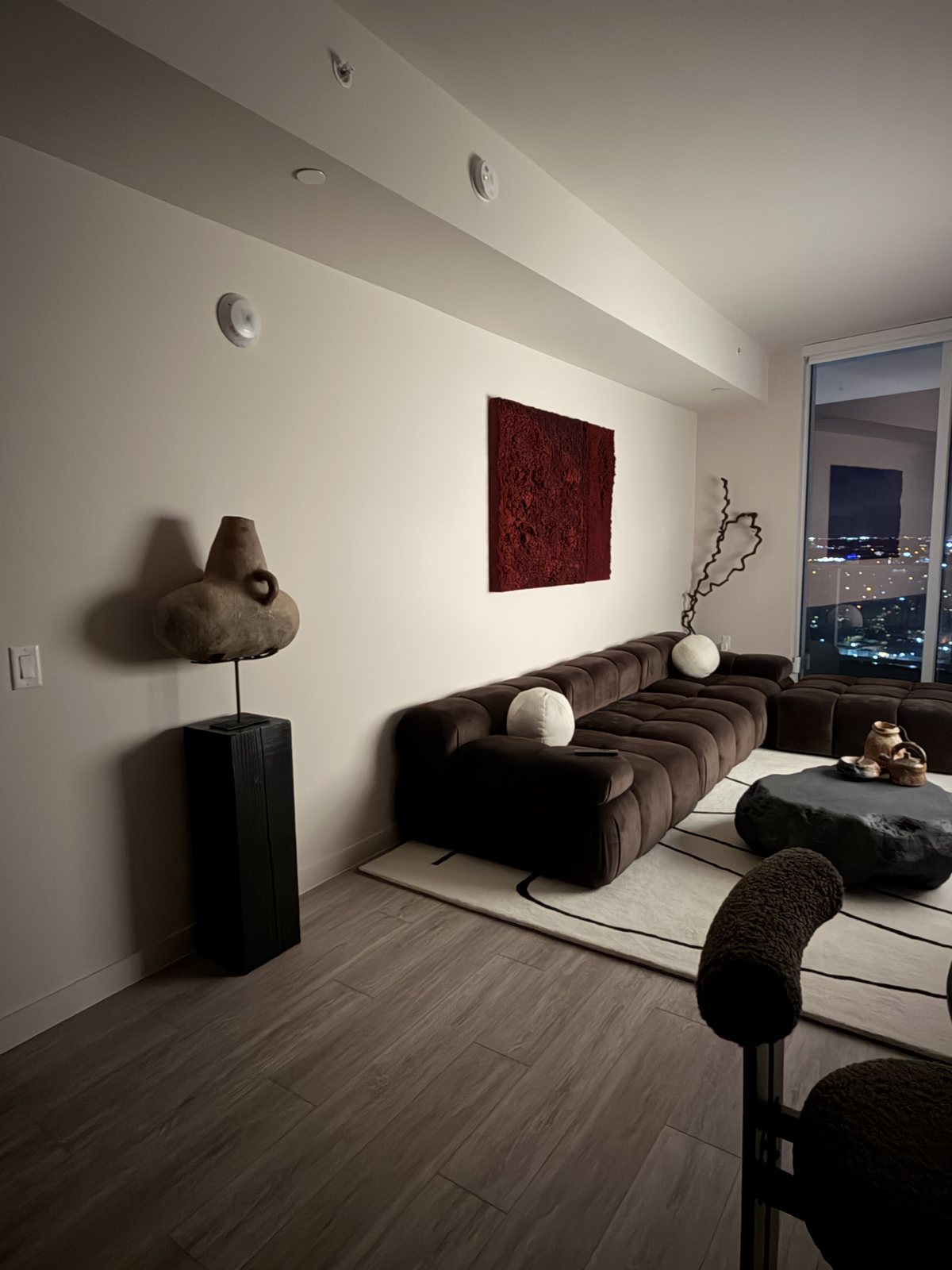 Black pedestal holding a sculptural vessel in a living room at night