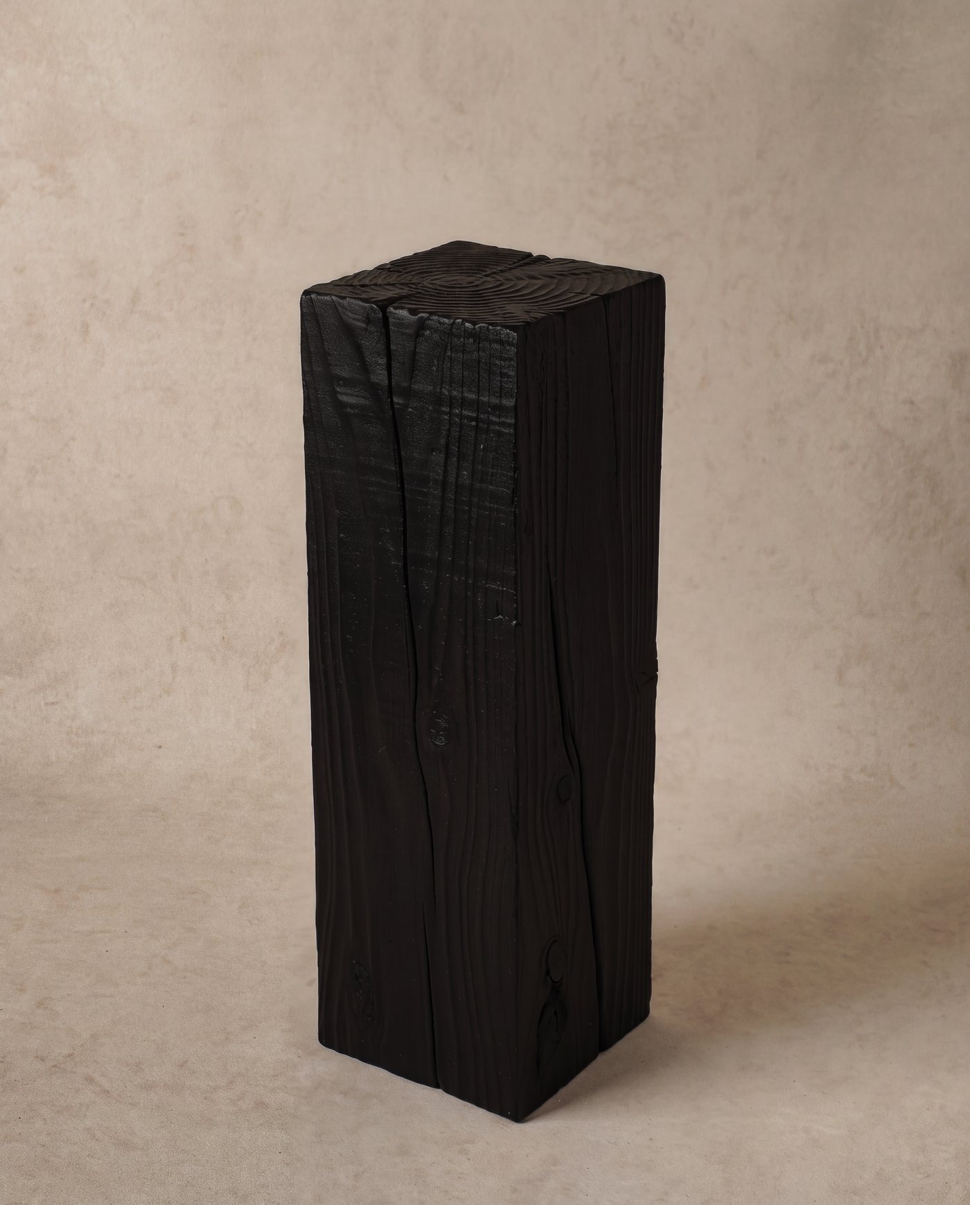 Black charred pedestal against a plaster backdrop